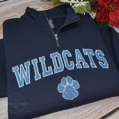 Navy blue pullover with 'WILDCATS' text and paw print on a wooden surface with flowers.