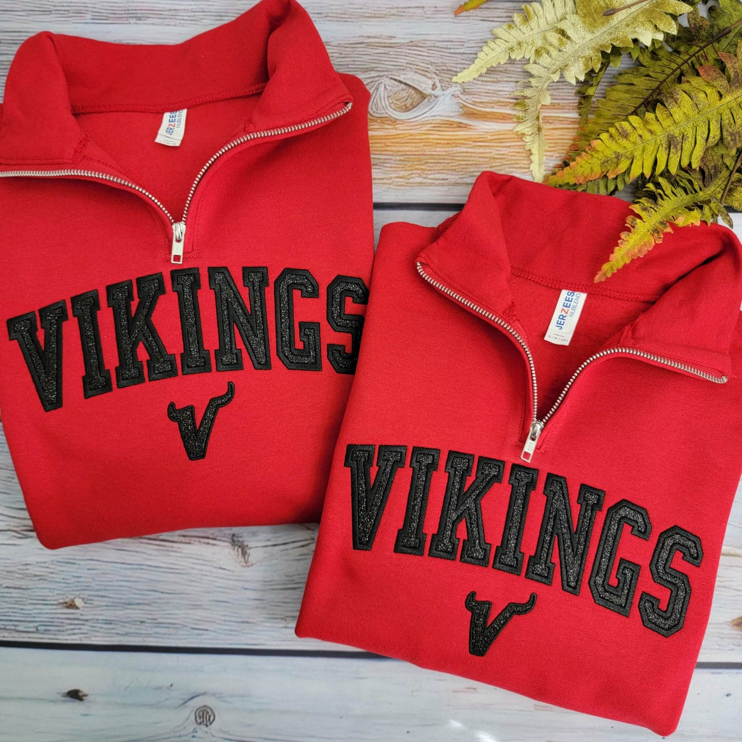 Two red 'VIKINGS' sweatshirts on a wooden surface with a plant in the background.