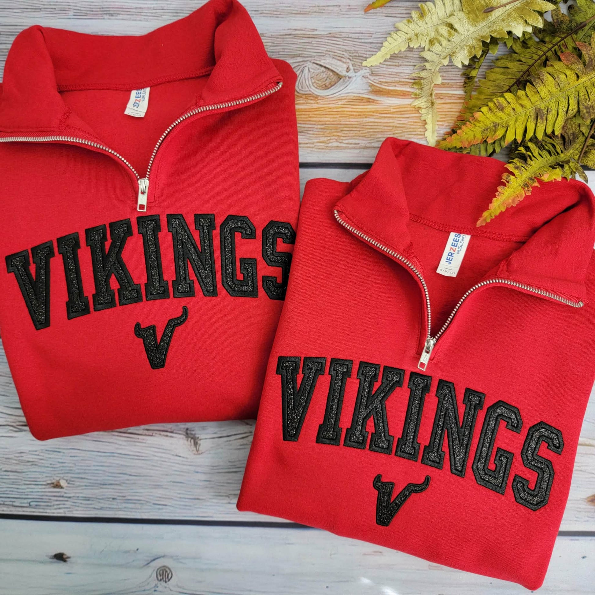 Two red 'VIKINGS' sweatshirts on a wooden surface with a plant in the background.