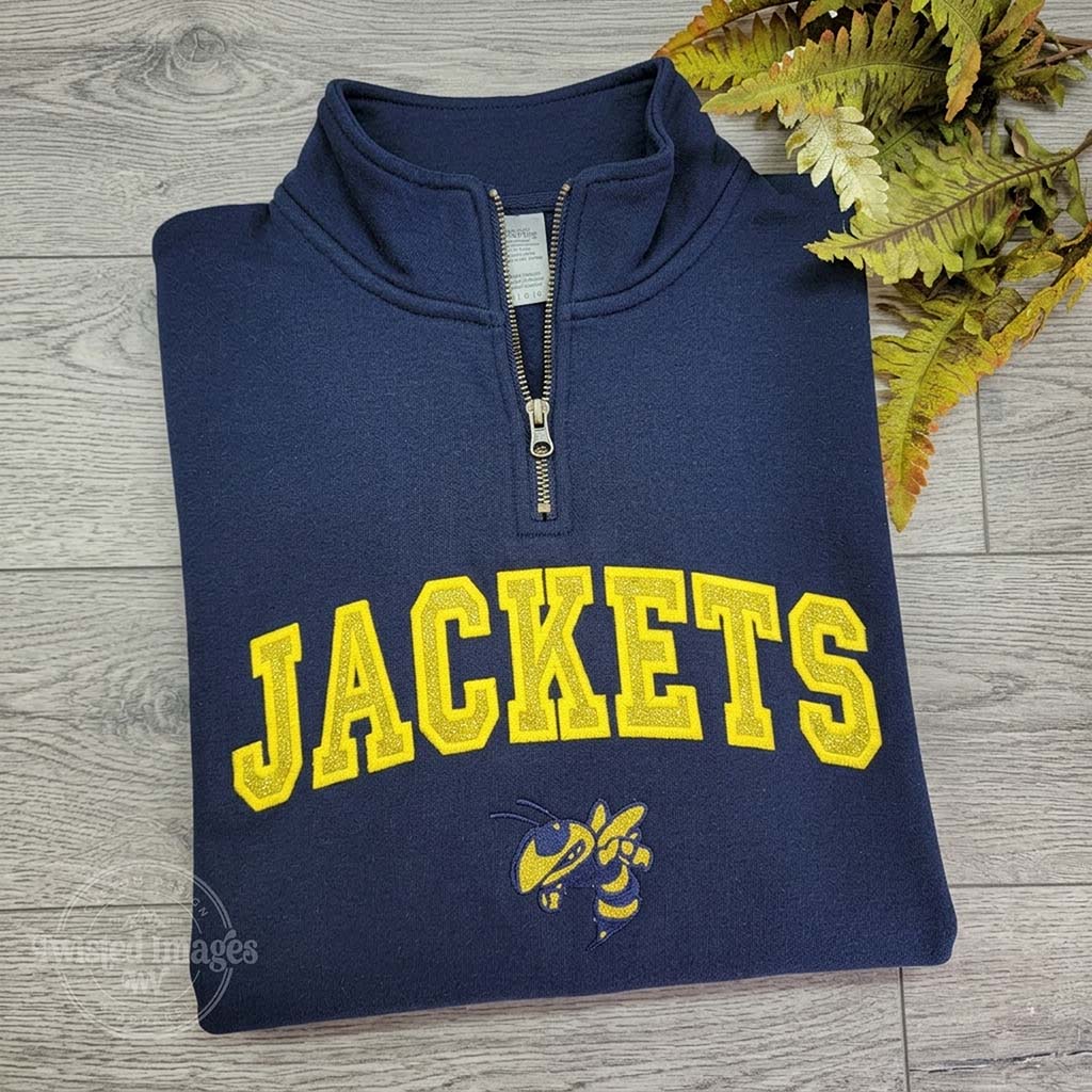 Navy blue sweatshirt with 'JACKETS' in yellow on a wooden surface with leaves.